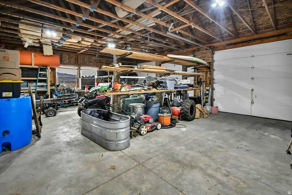 Spacious garage featuring a concrete floor, exposed wood beam ceiling, large roll-up door, and multiple windows