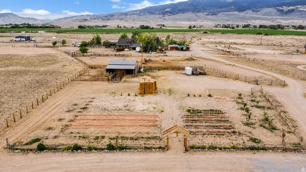 Expansive rural property featuring a large garden area with raised beds, a wooden garden archway, a barn structure with a metal roof, extensive fencing, and distant mountain backdrops