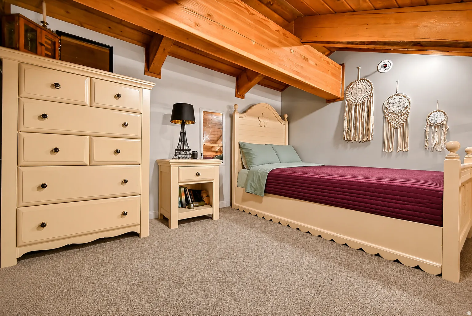 Exposed wood beams complement the neutral wall color in this room featuring a carpeted floor, built-in ceiling light, and a dedicated wall outlet