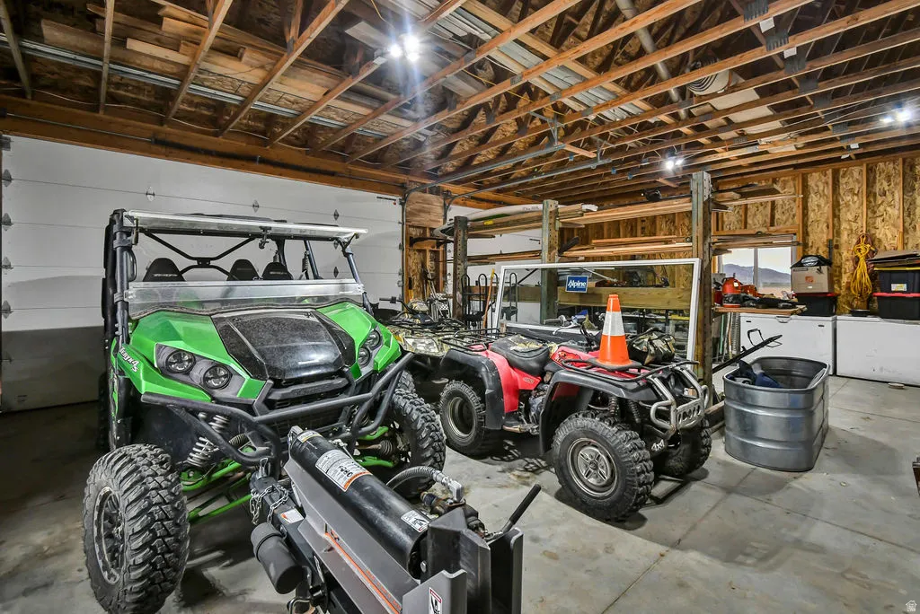 Spacious garage featuring exposed wood beam ceiling, concrete flooring, overhead fluorescent lighting, and two overhead garage doors