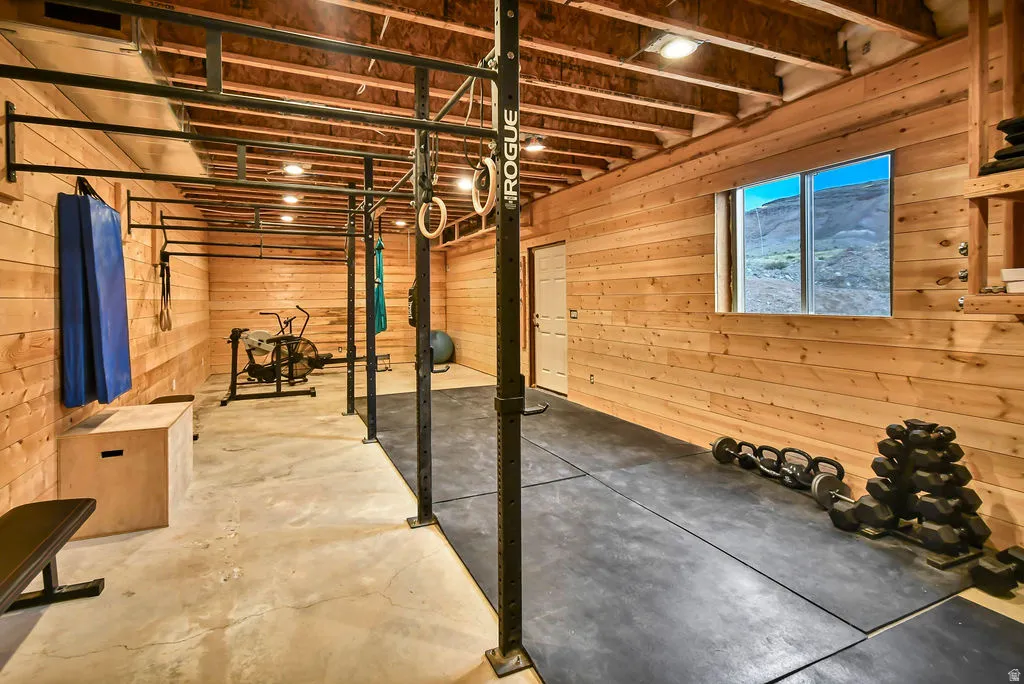 Dedicated fitness space featuring wood-paneled walls, exposed ceiling joists, and concrete flooring