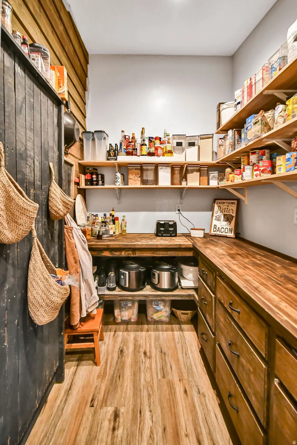 Expansive pantry featuring wood-finish flooring, custom wood cabinetry, extensive open shelving, and butcher block countertops