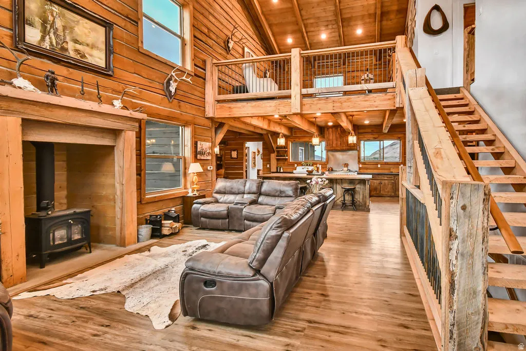 Spacious open-concept interior featuring wood-finish flooring, exposed wood beams, a wood-burning stove, a kitchen island, and an open loft area
