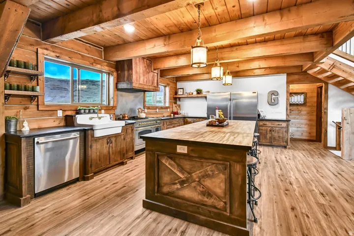 Open-concept kitchen featuring wood-finish flooring, exposed wood beam ceiling, custom wood cabinetry, a central island with bar seating, and stainless steel appliances
