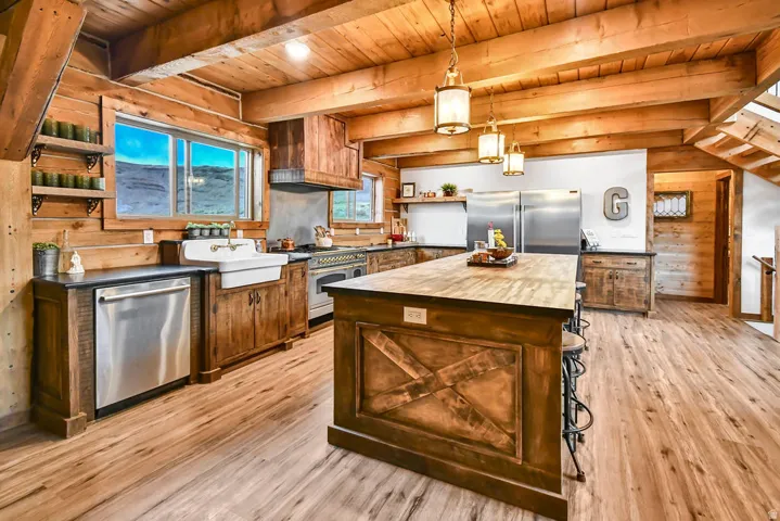 Kitchen featuring wood-finish flooring, exposed wood beams, wood cabinetry, a large kitchen island with a wood countertop, and stainless-steel appliances including a double-door refrigerator, dishwasher, and range