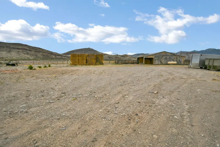 Expansive gravel lot featuring a large barn, visible fencing, and mountainous terrain in the background