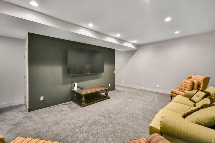 Spacious room featuring plush gray carpeting, recessed ceiling lighting, a dark accent wall, and white baseboards