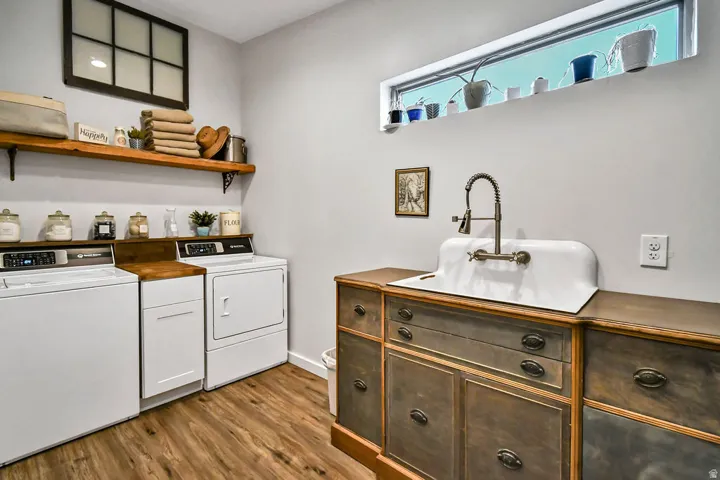 Utility room featuring wood-finish flooring, a white porcelain utility sink with a wall-mounted faucet, and a countertop with integrated cabinetry