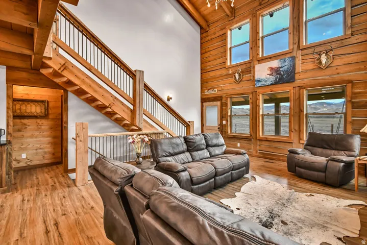 Vaulted ceiling living area featuring a prominent wood staircase with metal balusters, wood-finish flooring, and a log wall