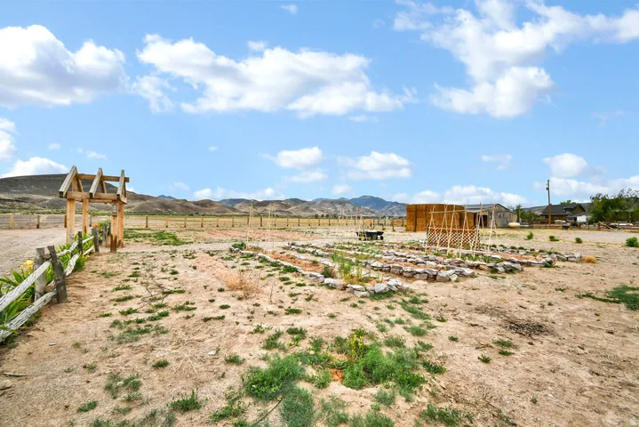 Expansive outdoor grounds featuring a split-rail fence, a wooden garden archway, and defined garden beds with stone borders
