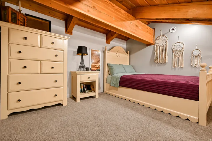 Exposed wood beams complement the neutral wall color in this room featuring a carpeted floor, built-in ceiling light, and a dedicated wall outlet