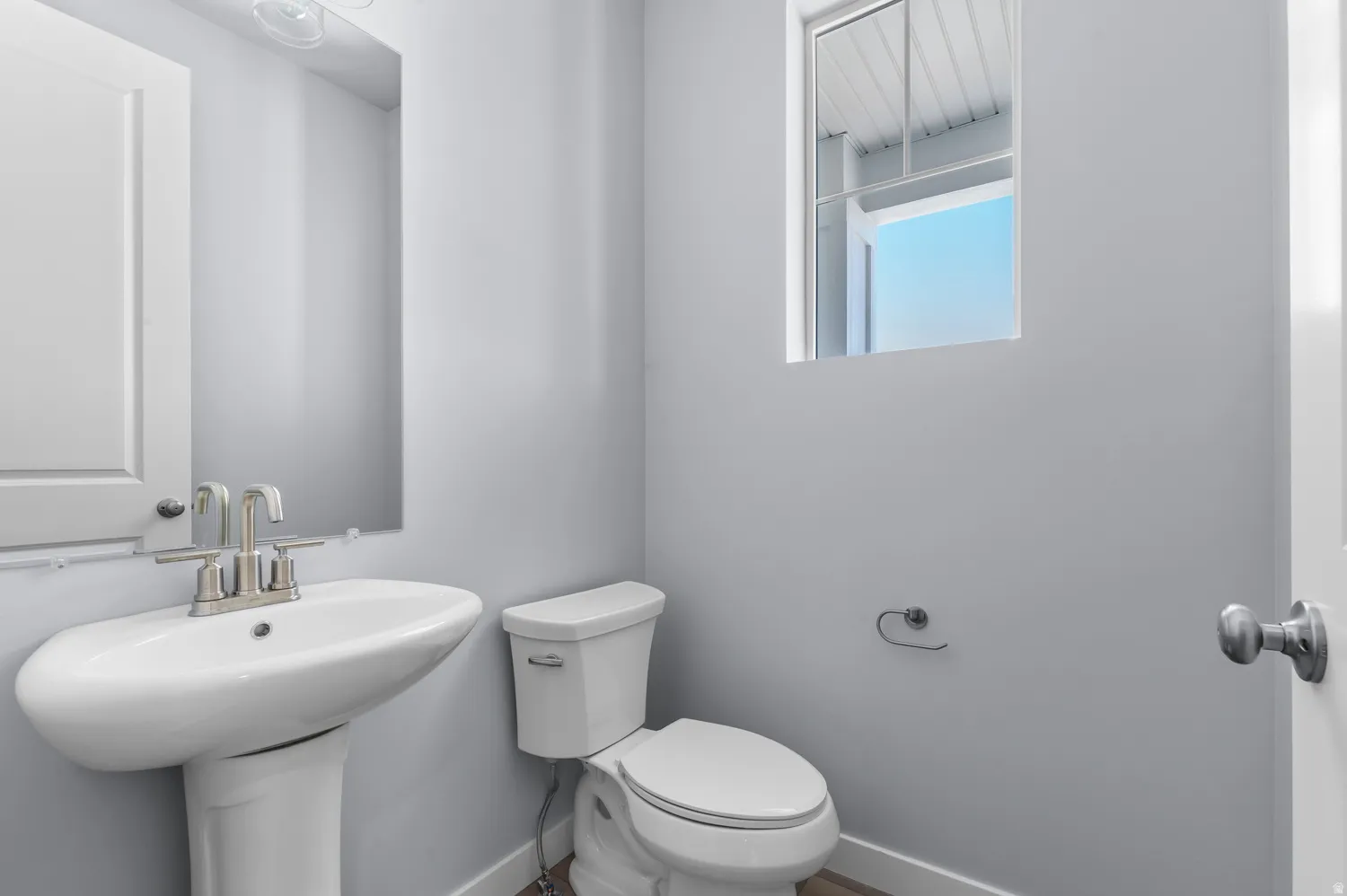 Pedestal sink with brushed nickel faucet, mirror, and white toilet