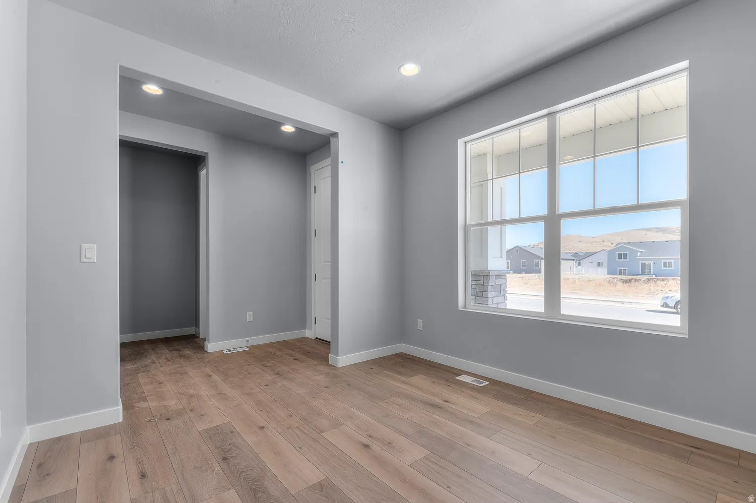 Spacious room featuring wood-finish flooring, a large multi-pane window, recessed lighting, and crisp white baseboards