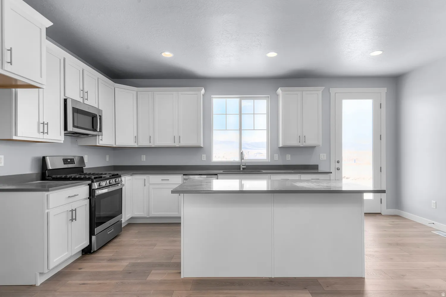 Bright kitchen featuring white shaker cabinetry, stainless steel appliances, a center island, and wood-finish flooring