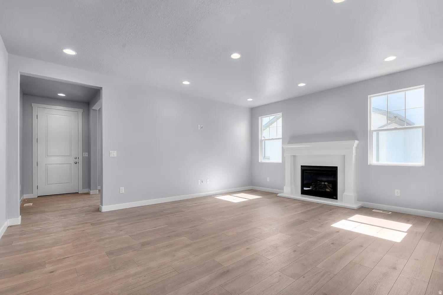 Spacious interior room featuring wood-finish flooring, recessed lighting, and a white mantel fireplace