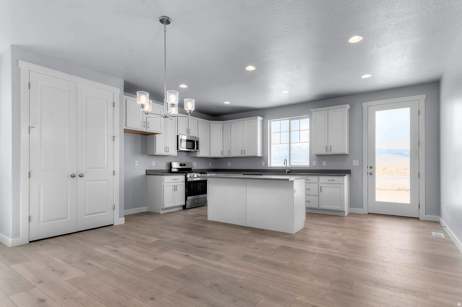Spacious kitchen featuring white cabinetry, a center island, stainless steel appliances, wood-finish flooring, and recessed lighting