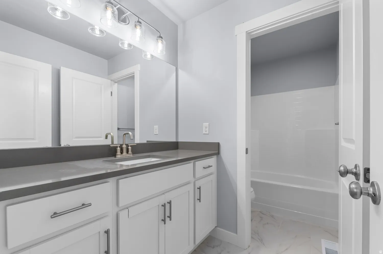 Bathroom vanity featuring a quartz-finish countertop and white shaker-style cabinetry