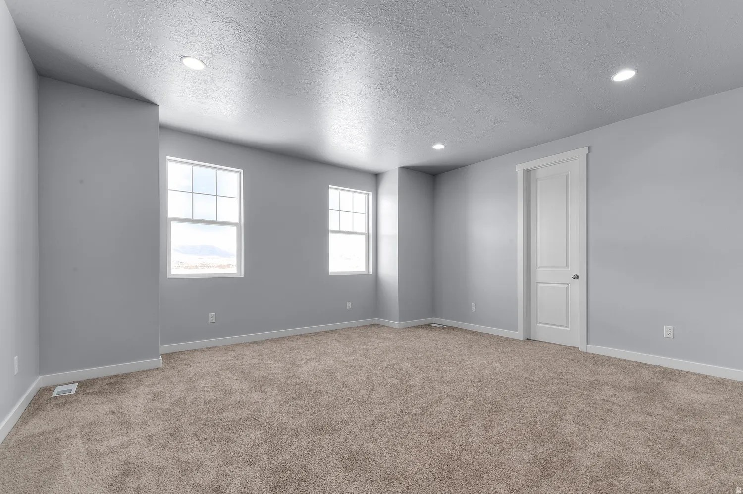 Expansive room featuring neutral-toned carpeting, two white-trimmed windows, a two-panel interior door, recessed ceiling lighting, and white baseboards
