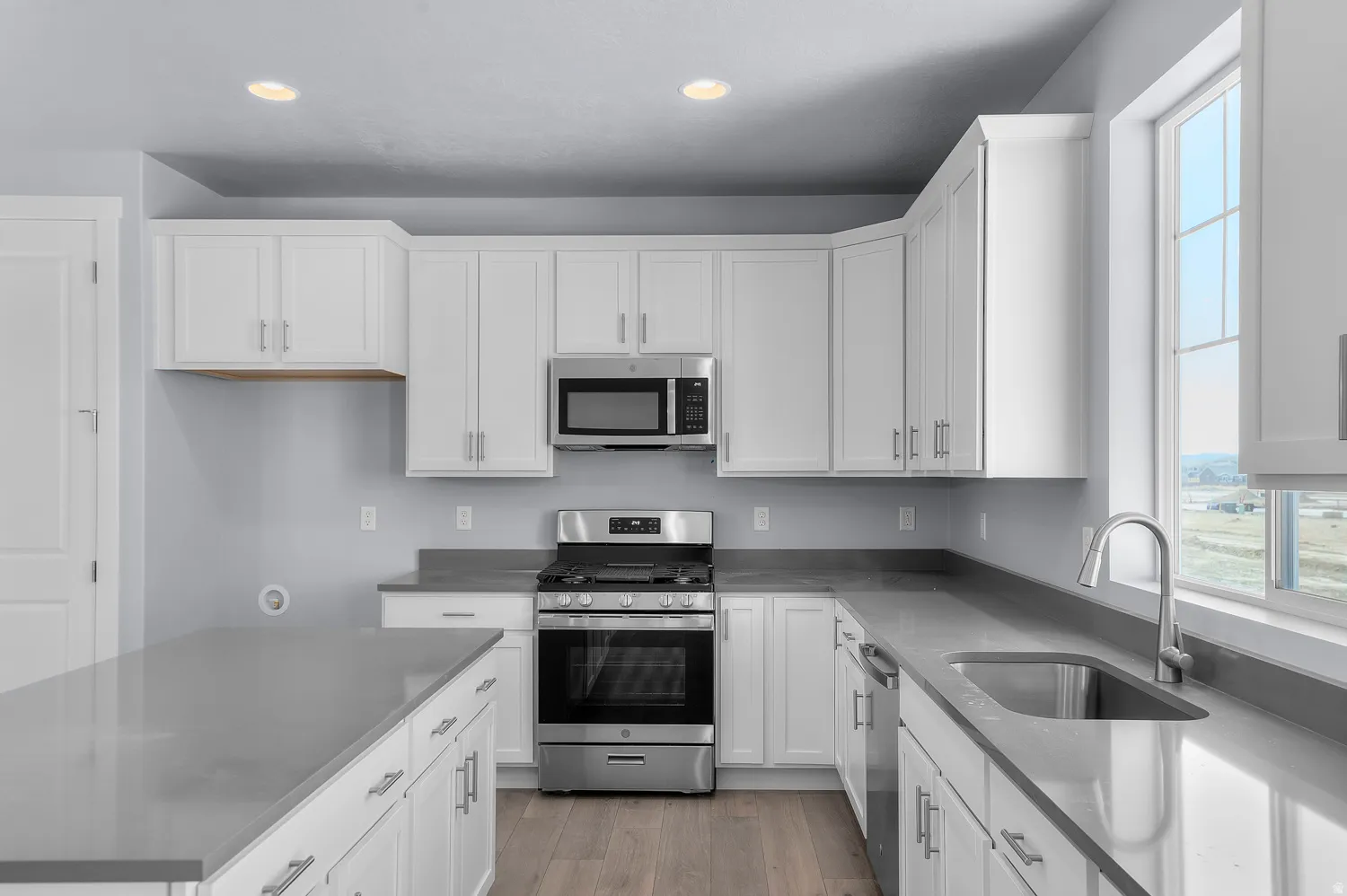 Bright kitchen featuring white shaker cabinetry, stainless steel appliances, a large window, recessed lighting, and wood-finish flooring