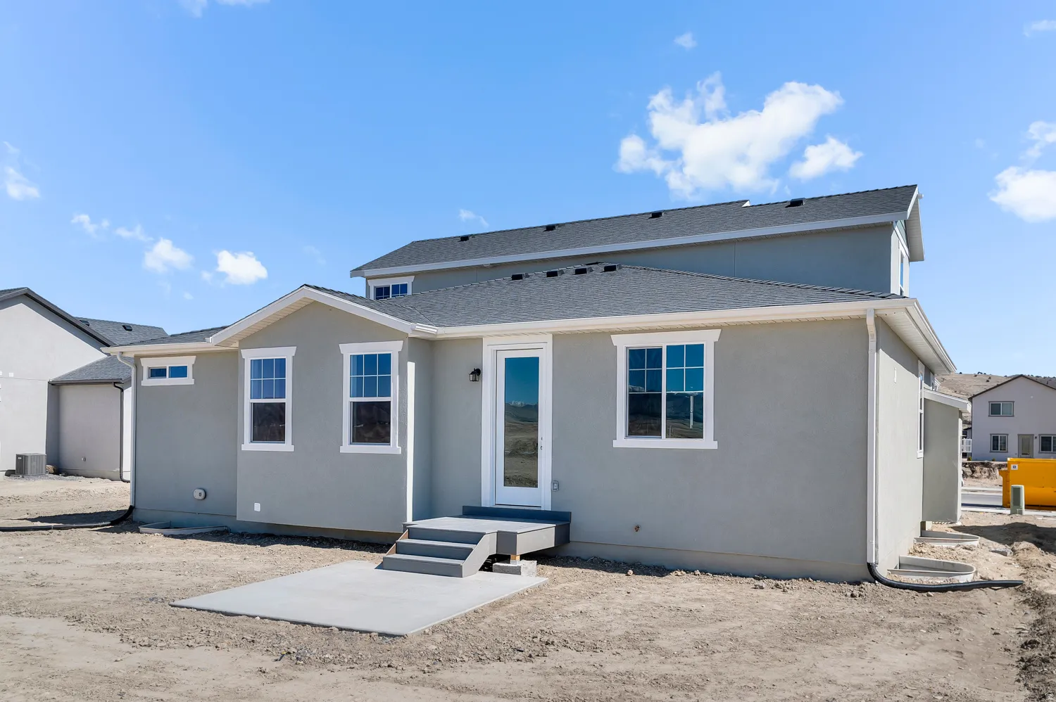 Multi-level residence featuring a light gray exterior, white trim windows, a rear patio with steps, and dark gray shingle roofing