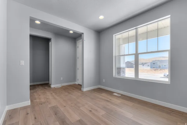Spacious room featuring wood-finish flooring, a large multi-pane window, recessed lighting, and crisp white baseboards