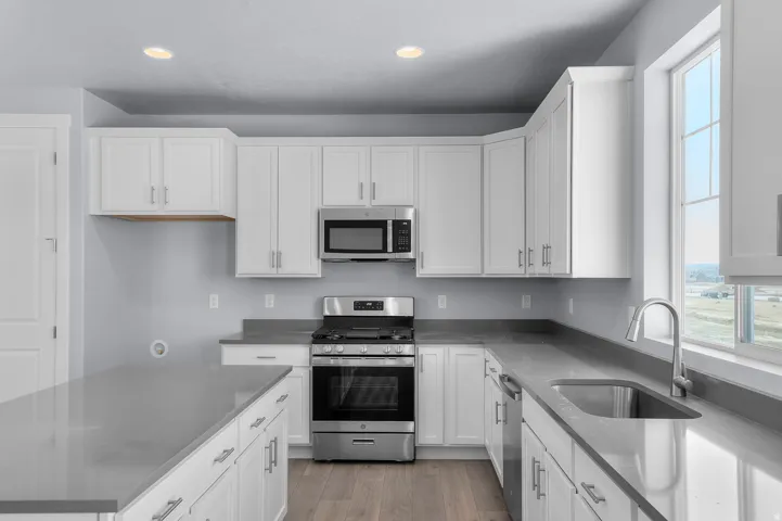 Bright kitchen featuring white shaker cabinetry, stainless steel appliances, a large window, recessed lighting, and wood-finish flooring