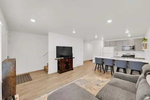 Open-concept living area featuring wood-finish flooring, recessed lighting, and a kitchen with light-colored cabinetry, stainless steel appliances, and a breakfast bar with seating