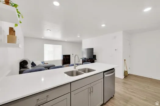 Kitchen island featuring a double-basin stainless steel sink, contemporary faucet, stainless steel dishwasher, and light gray cabinetry