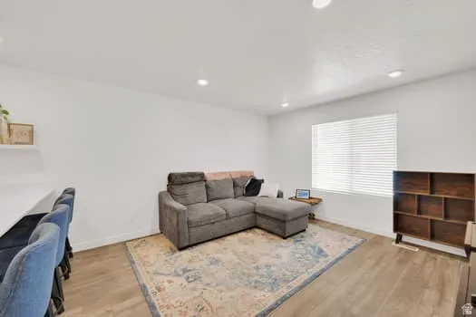 Open concept living space featuring recessed lighting, wood-finish flooring, a large window with horizontal blinds, and a built-in shelving unit