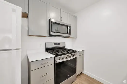 Kitchen featuring stainless steel appliances, light gray cabinetry, white countertops, and wood-finish flooring