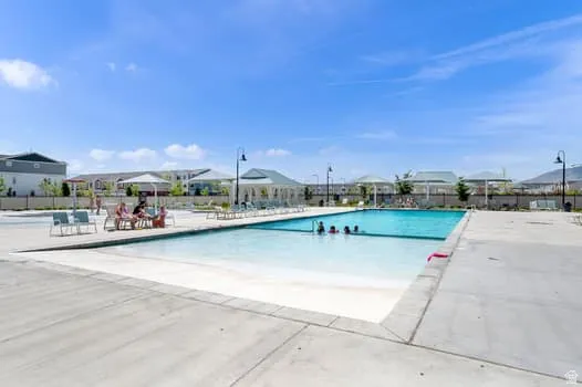 Community swimming pool featuring a concrete deck and multiple shaded seating areas