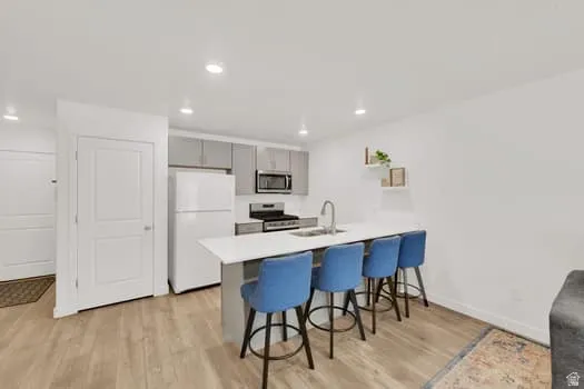 Kitchen featuring an island with seating, light gray cabinetry, white appliances, recessed lighting, and wood-finish flooring