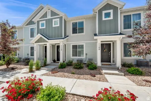 Modern townhome exterior featuring light-toned siding, dark entry doors, and a covered porch