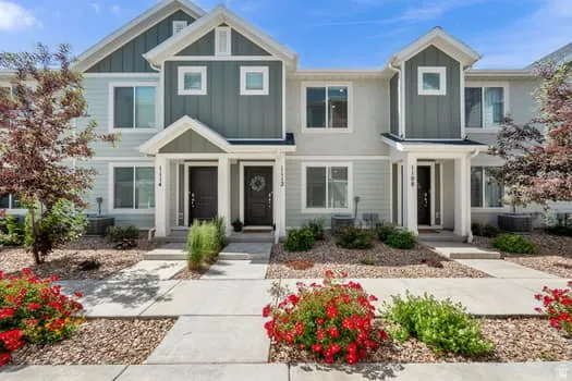 Contemporary townhouse exterior featuring light-colored siding with dark green accents, multiple windows, and covered entryways