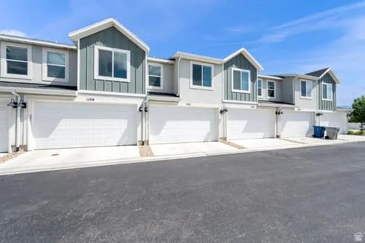 Row of modern townhomes featuring individual two-car garages and light gray stucco siding with contrasting vertical panel accents