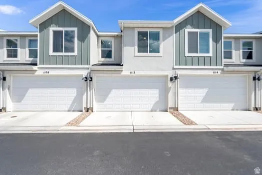 Contemporary townhome exterior featuring light gray stucco, green vertical siding accents, white trim, and a prominent gable roofline
