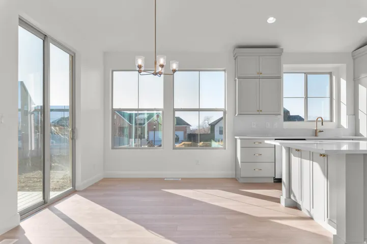 Open-concept living space featuring light wood-finish flooring, a contemporary chandelier, multiple windows, sliding glass patio doors, and a kitchen island with paneling
