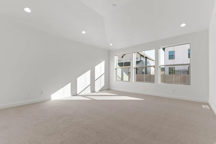 Spacious room featuring three large windows, recessed lighting, vaulted ceiling, and neutral-toned carpeting