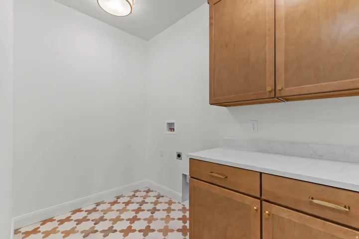 Laundry room featuring patterned floor tile, light wood-finish cabinetry, white countertop, and gold-tone hardware