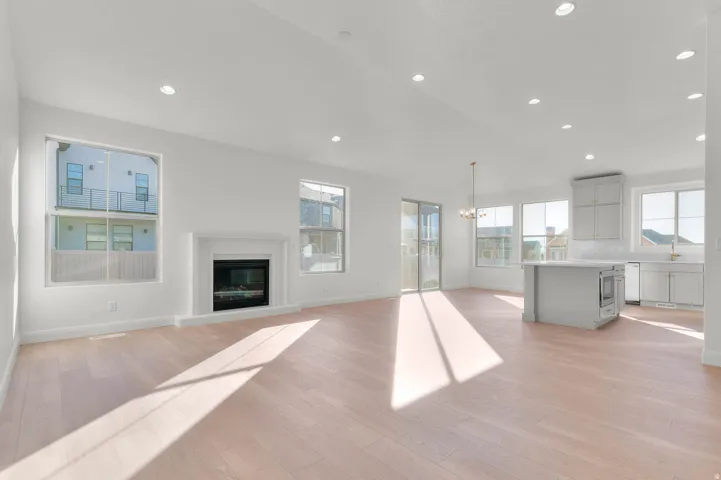 Open-concept living space featuring wood-finish flooring, recessed lighting, and a white fireplace with a classic mantel