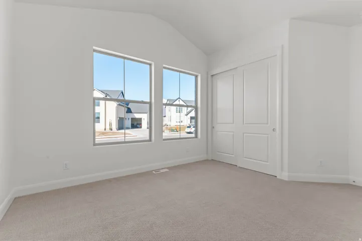 Vaulted ceiling room with two large windows, light neutral carpeting, white baseboards, and a double sliding door closet