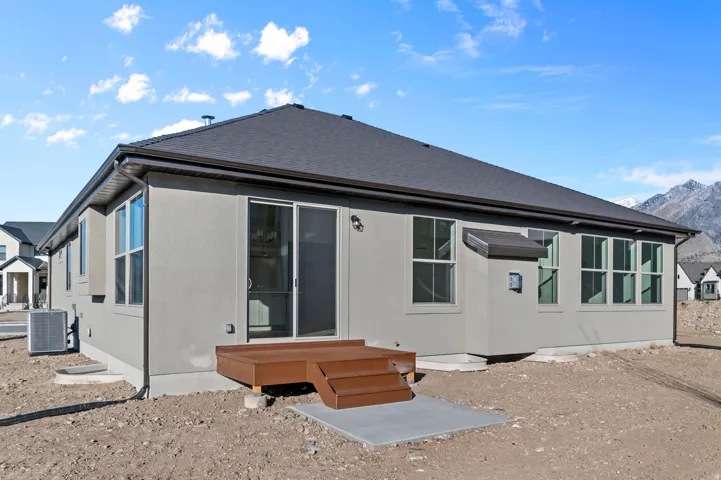Rear exterior featuring light stucco siding, a dark shingle roof, a sliding glass door, multiple large windows, and a raised wood-finish deck with steps