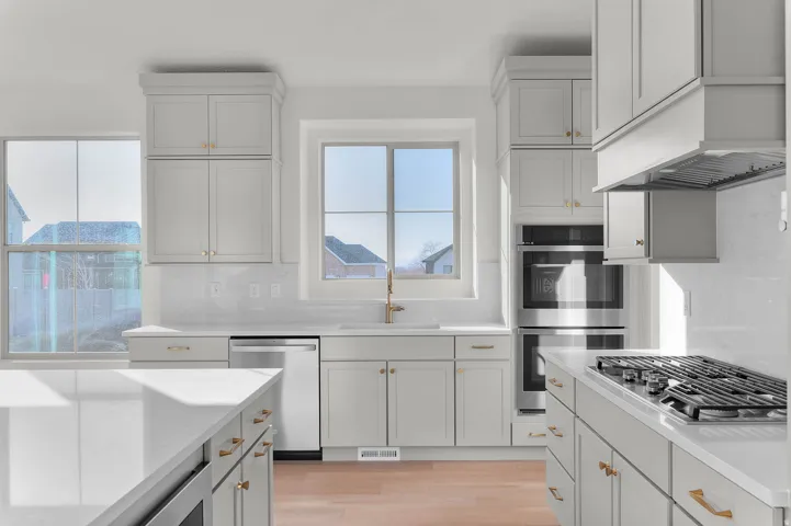 Contemporary kitchen featuring light-toned cabinetry with gold-toned hardware, white countertops, a built-in double oven, and a gas cooktop