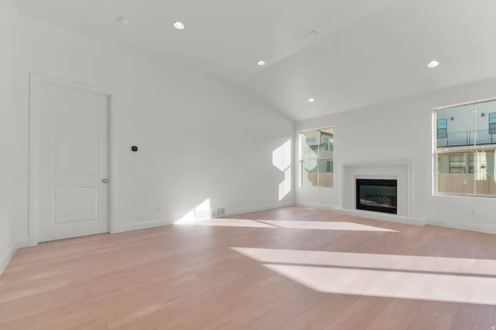 Bright living space featuring a gas fireplace with a white mantel, vaulted ceilings, recessed lighting, and light wood-finish flooring
