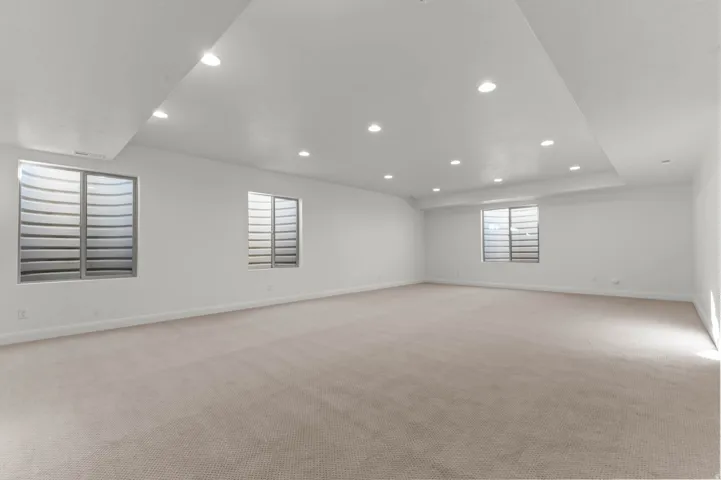 Spacious room featuring neutral carpeting, recessed lighting, white walls, and multiple egress windows with window well grates