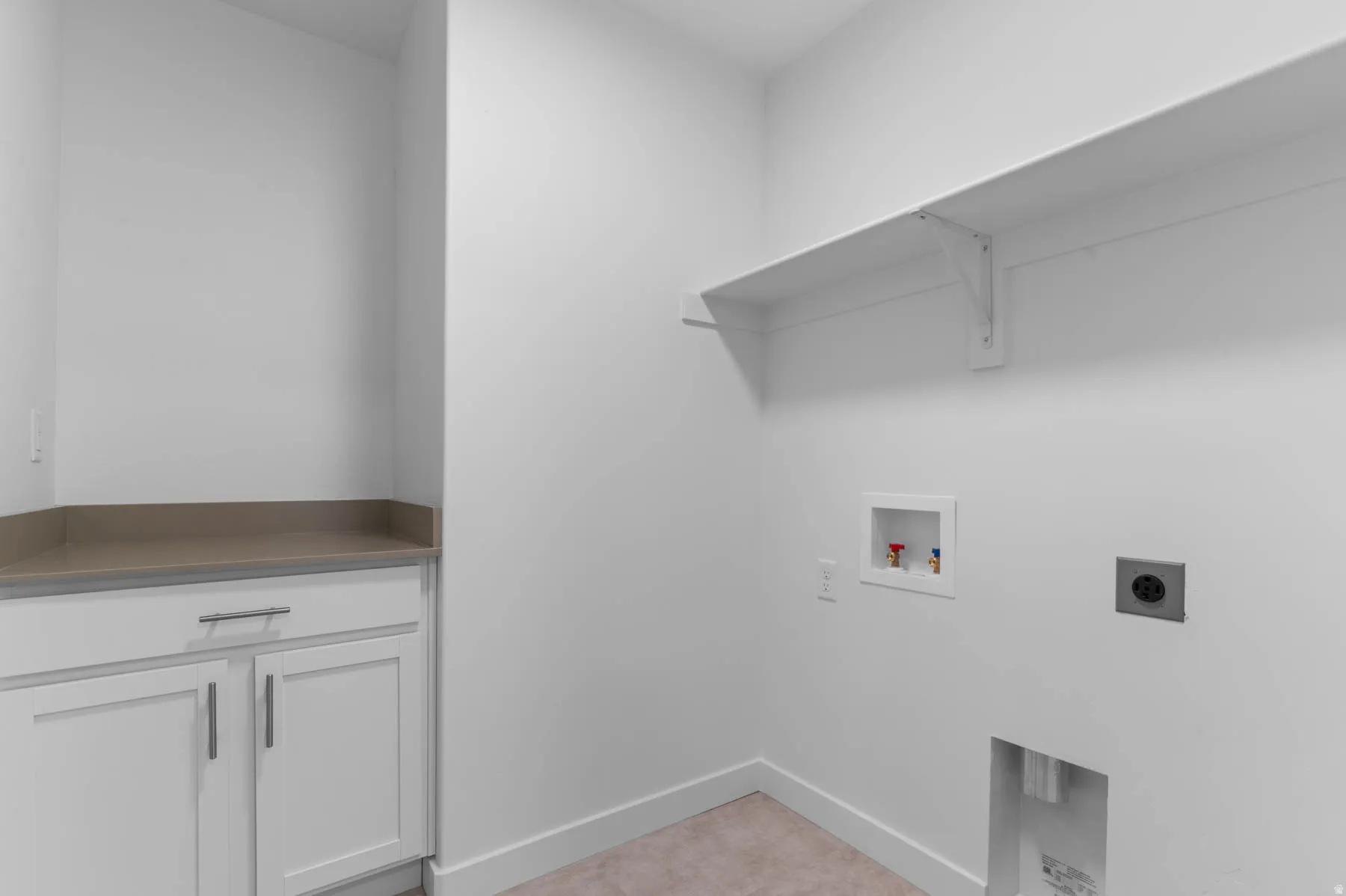 Dedicated laundry space featuring a built-in shelf, white cabinetry with brushed nickel hardware, and a neutral countertop
