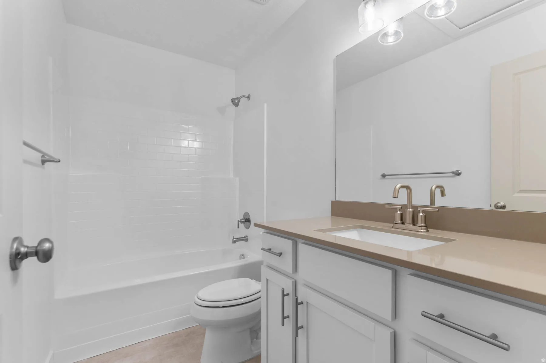 Bathroom featuring a white subway tile tub surround, white vanity cabinetry with brushed nickel hardware, light-toned countertop, and dual-handle faucet