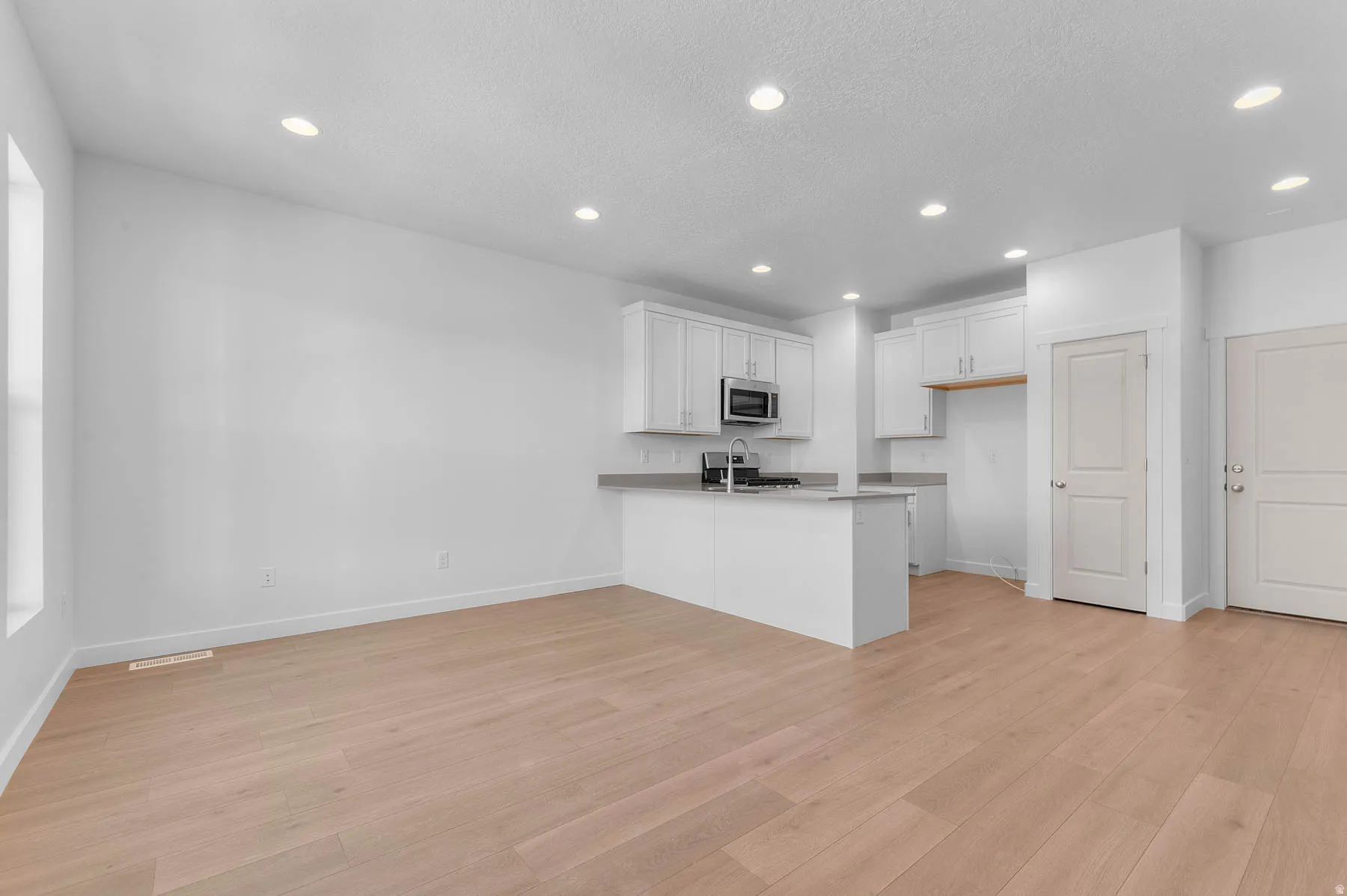 Open-concept living space featuring wood-finish flooring, recessed lighting, and a kitchen with white cabinetry, a stainless steel microwave, and a kitchen island