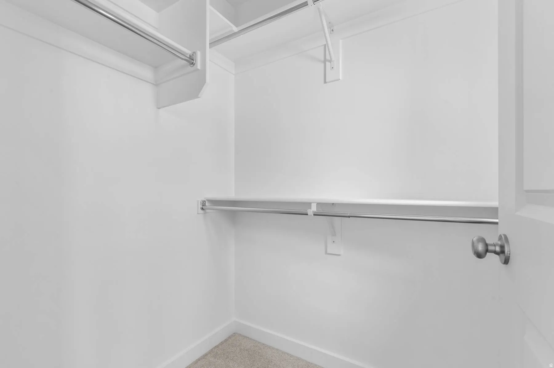 Walk-in closet featuring white painted walls, a light gray carpeted floor, and multiple metal hanging rods