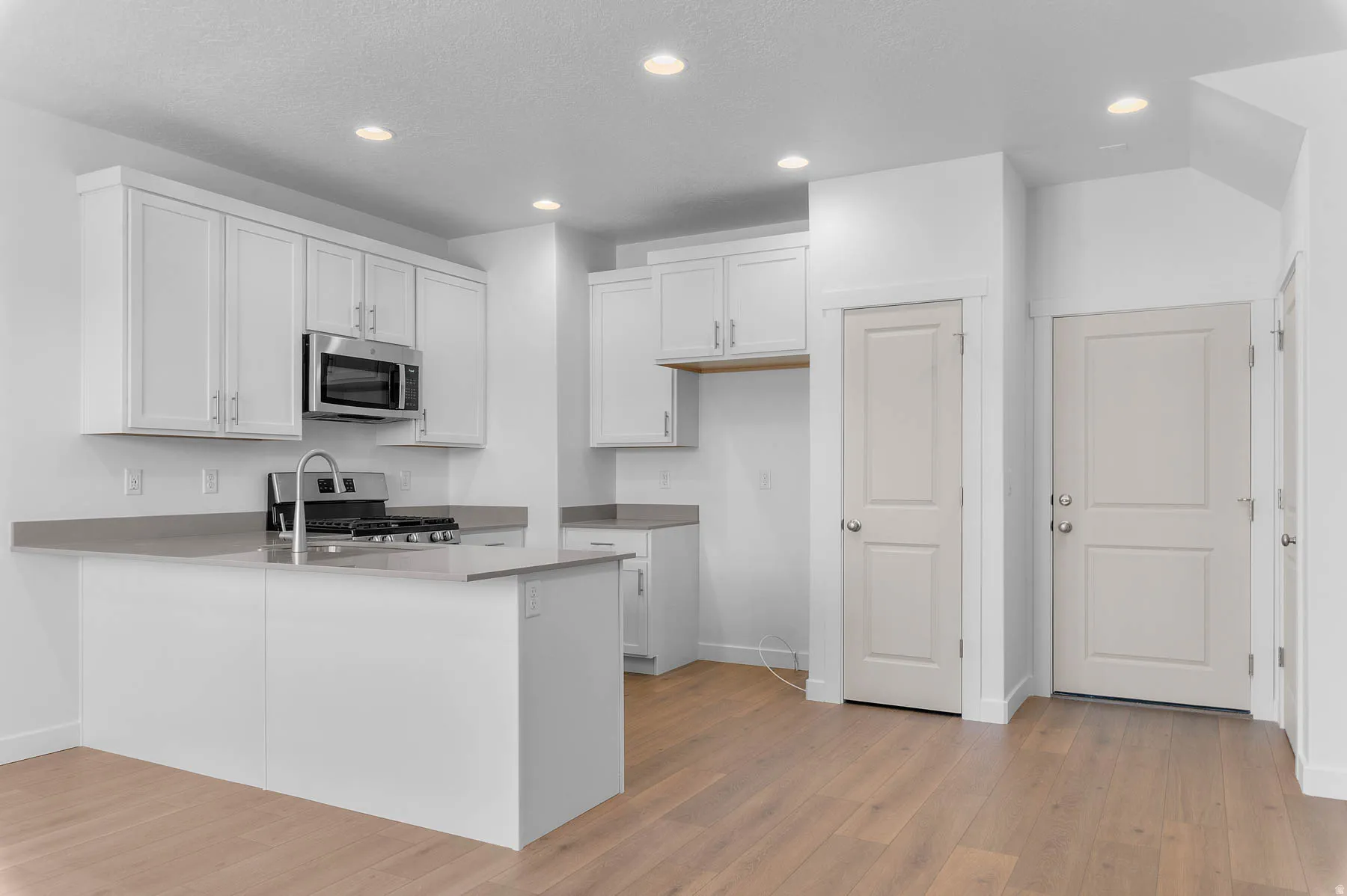 Contemporary kitchen featuring white cabinetry, stainless steel microwave, gas range, and a kitchen island with an integrated sink and chrome faucet